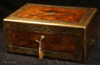 JB508: A very fine brass edged and inlaid  figured rosewood box ,  working Bramah lock, and having the Amorial crest for Fraser. The foliated borders are exceptionally well designed and executed with looping stems arranged in a mirror image fashion. The two sides of the pattern are separated by a palmette motif. The palmette is repeated as the central motif on the sides of the front of the box. The corners are inlaid with squared leaf designs. The severity of the lines, the arrangement of the design and the palmettes, are rooted in the neoclassical tradition.  The box has a compartmentalized leather and velvet lined interior with liftout tray. There is a hidden compartment with an unusual  secret release mechanism. The box also also has a drawer  fitted for jewelry which is secured shut by both a  brass pin and a lock. Circa 1820. Enlarge Picture
