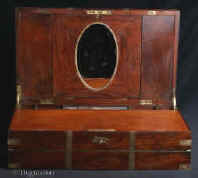 WB479: Early 19th Century brass bound solid flame mahogany triple opening writing box with unusual features such as visible dovetail construction. It opens up to a green baize writing surface a high back with central oval framed mirror, spaces for storing papers, compartments for pens, inkwell and pounce pot, and other writing accessories. There is a nest of secret drawers under the pen tray.Circa 1830. 