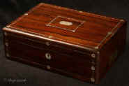 WB485:  Antique writing box veneered with figured rosewood with rounded edges, and countersunk brass carrying handles, inlaid to the top and front with white metal and mother of pearl accents opening to an embossed faded velvet writing surface and compartments for writing implements and paper.  Circa 1825. Enlarge Picture