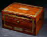 JB408: Regency box veneered in figured rosewood and decorated with strips of brass with cut out star motifs. Symmetrical restrained decoration of this type is typical of the early part of the 19th century. The box has a lower pull-out drawer with a central brass handle. The top part interior has been separated and lined. The leather cover on the envelope compartment on the inside top lid is original and it is embossed in a neoclassical design incorporating anthemia and palmettes. When it is folded down it reveals a mirror. The mirror is a new addition, although it sits in the alcove originally intended for a mirror. Some cracking to top veneer. The box has a working lock and key. Circa 1815. Enlarge Picture