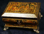 SB425:  Sewing box with  Japanned, raised and polychromed decoration on this sewing box depicting  a truly golden vision of Cathay. Figures relax in a garden with a distant rock in the background and the ho-ho bird above. This is a relatively late example of such work and it does not have an overall varnish. Note how the gold and the colors have remained brighter than in earlier examples. 8.5" wide.  Circa 1820. Enlarge Picture