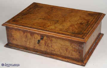 A mid 19th Century figured walnut box in Queen Anne style, the top base framed with an ogee molding. The top is inlaid with a framing of contrasting alternate boxwood and ebony lines and crossbandings in kingwood and burr walnut. The inside  is lined in red brocaded floral cloth.  The box has a working lock and key. Circa 1860. Enlarge Picture