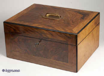  JB305: Antique box veneered with highly figured walnut, the top and front having a central panel framed by a crossbanding of straight grained walnut and having an inlayed brass line, the box opening to a velvet (replacement) lined liftout  tray. The inside of the lid is lined with lined with red satin which is button padded. There is a countersunk carrying handle to the top. The box is edged with ebony and has a working lock and key.  Circa 1890. Enlarge Picture