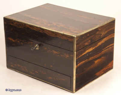 JB312: Antique box veneered in strongly figured  coromandel, on a mahogany construction with rounded brass edging to all sides,  and  working Bramah lock with key. The box is high quality, which continues into the interior. It is lined in velvet, and embossed leather. It has two  sprung drawers which are  fitted for jewelry released by pressing buttons,  Circa 1840. Enlarge Picture