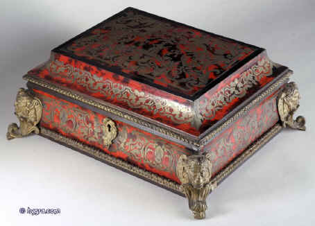 A shaped casket covered in boulle work of brass and red tortoiseshell,  with guilt ormolu mounts and feet. The pattern is in bold swirls forming floral designs and cusps typical of 18th century work.  The brass is engraved to give dimension to the design. The top is built around a stage where a musician sits playing his instrument. A complex composition, opulent and at the same time whimsical. The box is lined with silk.  Circa 1750 Enlarge Picture