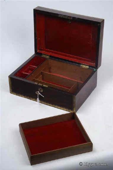 JB443: Rosewood and brass bound box circa 1820. A handsome box, veneered in saw-cut figured rosewood. It is edged in angled brass which defines its well proportioned form. A flat folding handle accents the top. The interior tray and dividing wooden sections are in mahogany and are contemporary with the box. The leather lining is original, but the velvet coverings have been added so as to protect and make the interior easier to use. These are removable. Both the working lock and the hinges are original.  Enlarge Picture