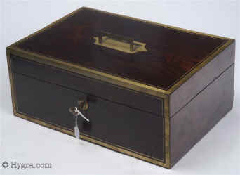  JB443: Rosewood and brass bound box circa 1820. A handsome box, veneered in saw-cut figured rosewood. It is edged in angled brass which defines its well proportioned form. A flat folding handle accents the top. The interior tray and dividing wooden sections are in mahogany and are contemporary with the box. The leather lining is original, but the velvet coverings have been added so as to protect and make the interior easier to use. These are removable. Both the working lock and the hinges are original. Enlarge Picture