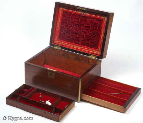 JB445: Figured Rosewood box edged in rounded brass circa 1850.  A three layered box with a lift out tray and a sprung side drawer. The tray has been fitted with velvet covers in order to protect the original surface whilst making the interior easier to use. The fold-down envelope on the lid retains its original ruched velvet and gold embossed leather framing. The rounded brass accents and protects the box and gives the corners a nice finish. Crack on veneer on top. Working lock and key. Enlarge Picture