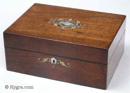 JB448: Rosewood veneered box with shell and brass inlays circa 1870: a very pretty box, the colour of the wood livened with a motif of stylized flora in abalone shell, mother of pearl and engraved brass. The escutcheon is designed in the same spirit with the central mother of pearl keyhole surround flanked by two elegantly curving leaves. The tray inside is added and the box has been relined. The back mirror with its gold embossed leather surround is original. Working lock and key. Enlarge Picture