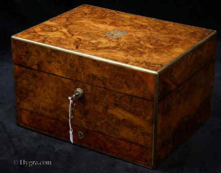 JB499: A high quality figured burr walnut dressing box with brass rounded edges and inlays  of brass working  Bramah lock with key,  the interior still fitted with dressing accessories in hobnail cut glass and hallmarked (1865) silver by John Harris. The box has a sprung lower drawer fitted for jewelry  which has its own lock.  There is silk lined document wallet in the lid behind a framed mirror. covered with ruched velvet on the other side. There is a lift out tray having further divisions and lids and a further compartment beneath for jewelry.1865. Enlarge Picture