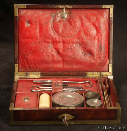 Description: JB502 A brass bound mahogany gentleman's campaign  dressing box by D. Edwards, Holborn, London the compartmentalized interior with supplementary lids, all  lined with red embossed Morocco leather and containing steel boot-strap pullers pewter containers for ointments and shaving soap (P & R Hendri)  a bone shaving brush,  razors, and for sharpening "S. ESTCOURT'S CRITERION STROP" Circa 1810. Enlarge Picture