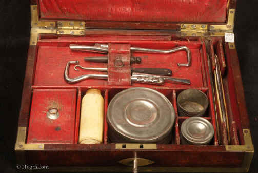 Description: JB502 A brass bound mahogany gentleman's campaign  dressing box by D. Edwards, Holborn, London the compartmentalized interior with supplementary lids, all  lined with red embossed Morocco leather and containing steel boot-strap pullers pewter containers for ointments and shaving soap (P & R Hendri)  a bone shaving brush,  razors, and for sharpening "S. ESTCOURT'S CRITERION STROP" Circa 1810.Enlarge Picture