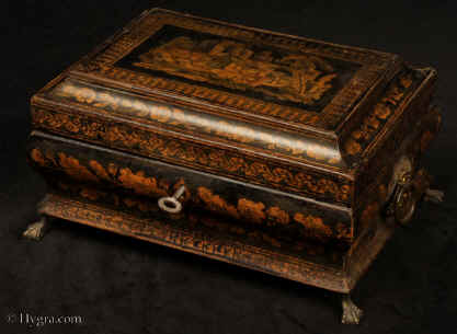 JB553:Shaped penwork box of complex casket form, the sides decorated with depictions of flora the top has a depiction of figures in front of a cottage with ruins in the background. The box has been relined and has a liftout tray. The box stands on clawed feet and has embossed gilded brass drop handles. Circa 1830. Enlarge Picture