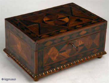 A box in various woods cut as very thick veneers. The woods are juxtaposed in an unusual pattern, which combines angular geometric shapes with hearts and a central  stylized flower. Origin: English. Circa: 1780 Enlarge Picture