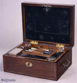 JB 185: Early 19th century Rosewood veneered  box with brass countersunk handles and subtle  accents. This box typifies the understated quality of the period. The interior is lined in velvet and leather in a color combination which is again typical of the time. The bottles have silver plated tops. It bears the Edwards label. Enlarge Picture