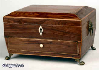  A shaped regency box veneered with kingwood and framed with boxwood having a compartmentalized upper part  and a lower drawer standing on cast paw feet and having gilded lion head drop handles circa 1815 Enlarge Picture