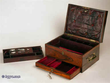  A Regency figured rosewood box, circa 1810, by Chrisp manufacturer,  of  Cockspur Street, London. The top has  ebony edges  and a brass plate; the sides have  inset brass carrying handles. The box also has a drawer of dovetail construction which is fitted for jewelry and separately locked. The upper part has a liftout tray which is covered with tooled leather. The tray has a supplementary lid containing modern  silver handled manicure  tools. Enlarge Picture