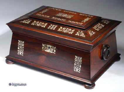 SB125: Antique  figured rosewood sewing box the top panel framed  inlaid with mother of pearl to the top and front having turned rosewood drop-ring handles and standing on  turned bun  feet. Inside the lid is lined with contrasting blue and cream silk and has a document wallet behind. The box has a liftout tray with supplementary lids covered in silk. Circa 1830. Enlarge Picture