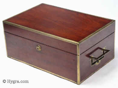 SB454: Mahogany and brass bound sewing box circa 1820. This is a most unusual early sewing box, both strong and robust. The high quality of the structure suggests that it was made to withstand travel as well as sit in elegant drawing rooms. The mahogany is edged in squared brass all around and bears flat-folding side handles. The original interior is lined in red textured leather. The tray is in keeping with the exterior and is structured for strength. The envelope is most unusual and opens with a silver catch. Some bending on bottom brass suggesting that the box did travel! Working Bramah lock and key.  Enlarge Picture