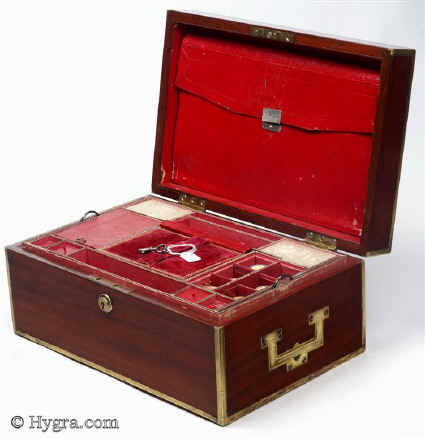 SB454: Mahogany and brass bound sewing box circa 1820. This is a most unusual early sewing box, both strong and robust. The high quality of the structure suggests that it was made to withstand travel as well as sit in elegant drawing rooms. The mahogany is edged in squared brass all around and bears flat-folding side handles. The original interior is lined in red textured leather. The tray is in keeping with the exterior and is structured for strength. The envelope is most unusual and opens with a silver catch. Some bending on bottom brass suggesting that the box did travel! Working Bramah lock and key.  Enlarge Picture