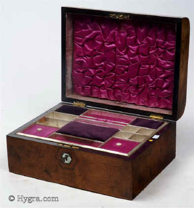 SB459: Burr walnut veneered box of rounded form, circa 1870. A box veneered in particularly well figured burr walnut. It is sparsely decorated with hexagons of mother of pearl subtly cross banded and framed in lines of contrasting woods. The tray, three silk covers and ruched back are original. The darker covers are of later velvet. Working lock and key.   Enlarge Picture