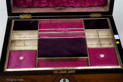 SB459: Burr walnut veneered box of rounded form, circa 1870. A box veneered in particularly well figured burr walnut. It is sparsely decorated with hexagons of mother of pearl subtly cross banded and framed in lines of contrasting woods. The tray, three silk covers and ruched back are original. The darker covers are of later velvet. Working lock and key.   Enlarge Picture