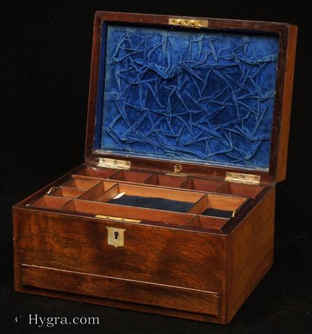 Antique Figured Rosewood box with lift-out compartmentalized tray and sprung drawer fitted for jewelry. There are mother of pearl escutcheons to the top and the front. There is a ruched velvet pad in the lid with mirror framed with gold embossed leather behind. It is released by pressing behind the lock catch. The sprung drawer is released by pressing on a button in the centre of the back facing. The lift-out tray is of mahogany construction with rosewood facings. New pads of velvet have been made to make the tray suitable for jewelry. There is further space beneath. Circa 1850.  Enlarge Picture