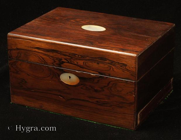 Antique Figured Rosewood box with lift-out compartmentalized tray and sprung drawer fitted for jewelry. There are mother of pearl escutcheons to the top and the front. There is a ruched velvet pad in the lid is framed with gold embossed leather behind. It is released by pressing behind the lock catch. The sprung drawer is released by removing a brass pin. The lift-out tray is of mahogany construction with rosewood facings. New pads of velvet have been made to make the tray suitable for jewelry. There is further space beneath. Circa 1840.  Enlarge Picture