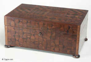 JB144: A refined Georgian box veneered with parquetry exploiting  subtle variations of wood color  and pattern. The woods are both native and imported hardwoods with some pieces  the added interest of end grain or oyster cut . The maker was exploring  geometry in wood and  may have been inspired by some of the mosaic inlay boxes being imported from India. There are different design on each side. The box stands on turned wooden feet has a working lock and key. Circa 1790. 
