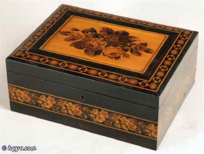 A rosewood veneered Tunbridge ware box by T Barton, the slightly domed top inlayed with a display of roses depicted in micro mosaic,  framed by bandings of contrasting light and dark wood and particularly well matched geometric micro mosaic; there is a further banding of Berlin wool work Design encircling the box. The inside is lined with its original red paper circa 1850 Enlarge Picture