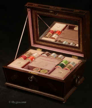 SB487: Antique  figured rosewood sewing box the top panel and base  framed by gadrooning, inlaid with mother of pearl to the top and front having turned rosewood drop-ring handles and standing on  turned bun  feet. Inside the lid is lined with  cream silk and paper. Inside the lid there is a mirror framed by gold embossed leather with a document wallet behind The box has a liftout tray with supplementary lids covered in silk. Circa 1830. 