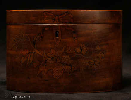 TC104: A fine inlaid harewood tea caddy of oval form the front directly inlaid with maple and fruit wood depicting a basket of fruit on trailing branches: grapes and cherries. The basket is suspended from a bow which is integrated within the design of the escutcheon. The lively composition is most unusual. The sensitive design and treatment of the escutcheon shows a mastery of form and purpose. The inlay is given further definition with fine engraved penwork. 1790. Enlarge Picture