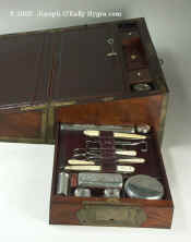 A Rare brassbound Captains box of beautifully figured mahogany, having a screw-down mechanism and fitted with dressing accessories by George Palmer. There are secret containers even in the back sections (rare), The part which meets in the middle when the box is opened to the writing position is thicker to accommodate these. The secret containers fit very snuggly in very precisely crafted spaces. The side drawer is fitted out as a dressing box. The tops of the glass jars are in silver, a most unusual feature in boxes of combined usage.  The silver bears the crest design of a horse in a central cartouche, an indication that it belonged to an officer of the cavalry. It bears hallmarks for 1829. A box of remarkable complexity and quality.