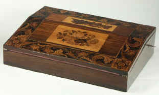 A Tunbridge ware writing slope veneered with rosewood and decorated with micro mosaic depicting floral subjects. The framing band of the top has a flowing design and is expertly and beautifully executed.  Unusually for Tunbridge ware the corner detail are very carefully designed so that there are no abrupt joins in the pattern the four corner squares of formal micro mosaic harmonize with the lively longer pattern but also provide strong punctuation to the piece. The careful design and execution and the use of rosewood veneer point to an early example of such work.  The box also features a pair of original inkwells with turned Tunbridge stick-ware tops.